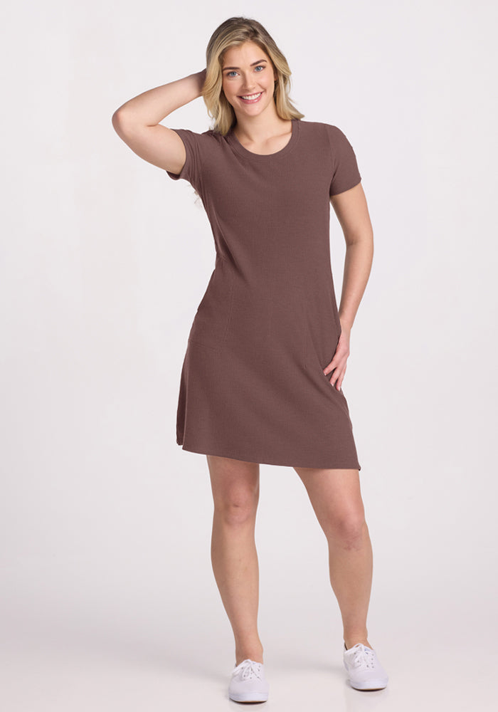Woman in a Woolx Harlowe Ribbed Dress - Peppercorn smiles with one hand on her head, wearing white sneakers.