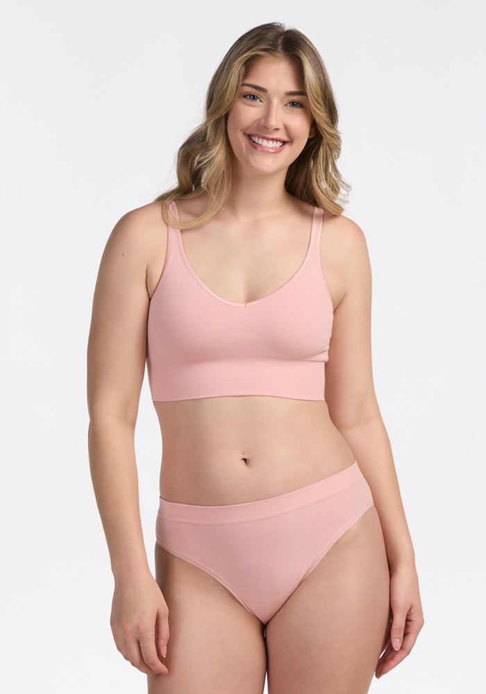 A woman with long, wavy blonde hair smiles while wearing the Woolx Hayden Bra in Rosewater against a plain white background.
