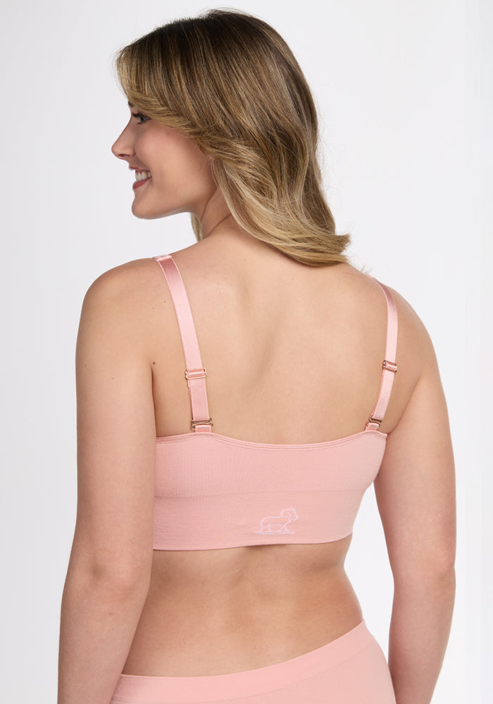 A woman with shoulder-length blonde hair is shown from the back, wearing the Woolx Hayden Bra in Rosewater, featuring adjustable straps, moisture-wicking fabric, and a small white dachshund outline on the back.