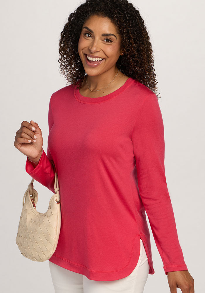 Smiling woman with curly hair wears the Woolx Hazel Tunic in Berry Ice Pop and holds a cream-colored woven handbag.