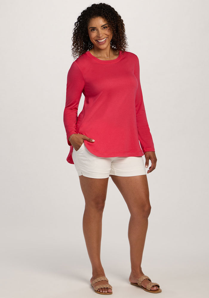 Woman smiles in the Woolx Hazel Tunic - Berry Ice Pop, white shorts, and sandals against a plain background.