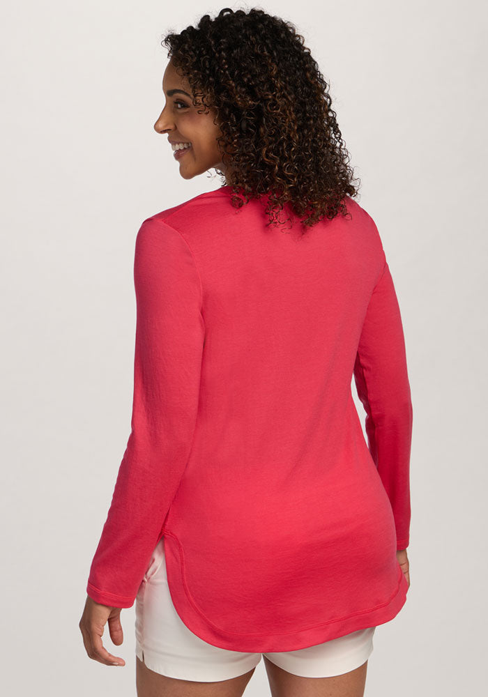 Woman with curly hair wearing the Woolx Hazel Tunic in Berry Ice Pop and white shorts, facing away and smiling.