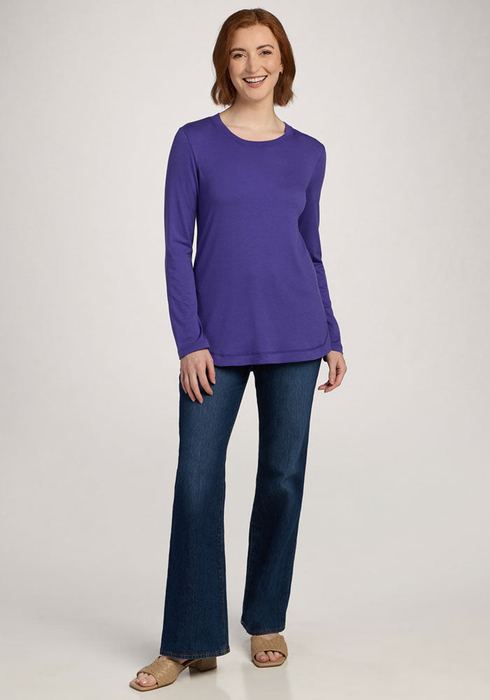 Woman smiling in the Woolx Hazel Tunic - Berry Indigo, blue jeans, and tan sandals against a plain background.