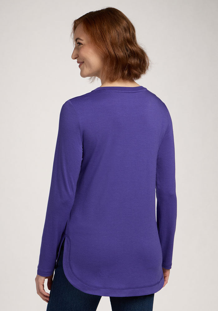Woman with short auburn hair wears the Woolx Hazel Tunic in Berry Indigo, seen from the back, smiling left.