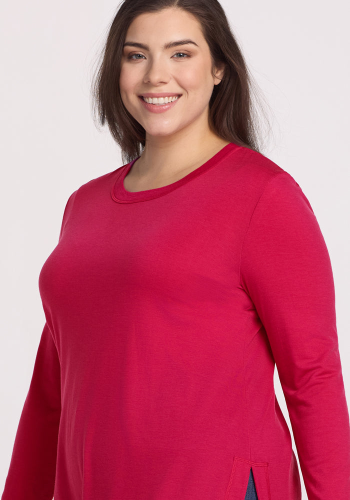A woman with long brown hair smiles, wearing the Woolx Hazel Tunic in Poppy Spark against a light background.
