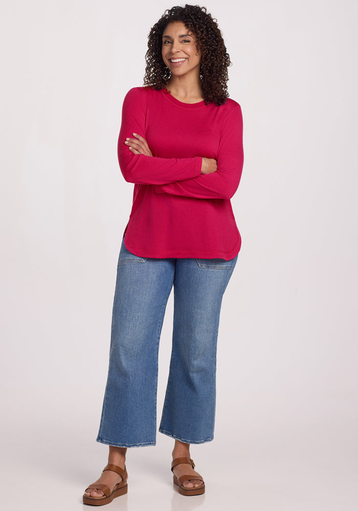 Woman with curly hair smiles in a Woolx Hazel Tunic in Poppy Spark, blue jeans, and sandals. Final Sale.