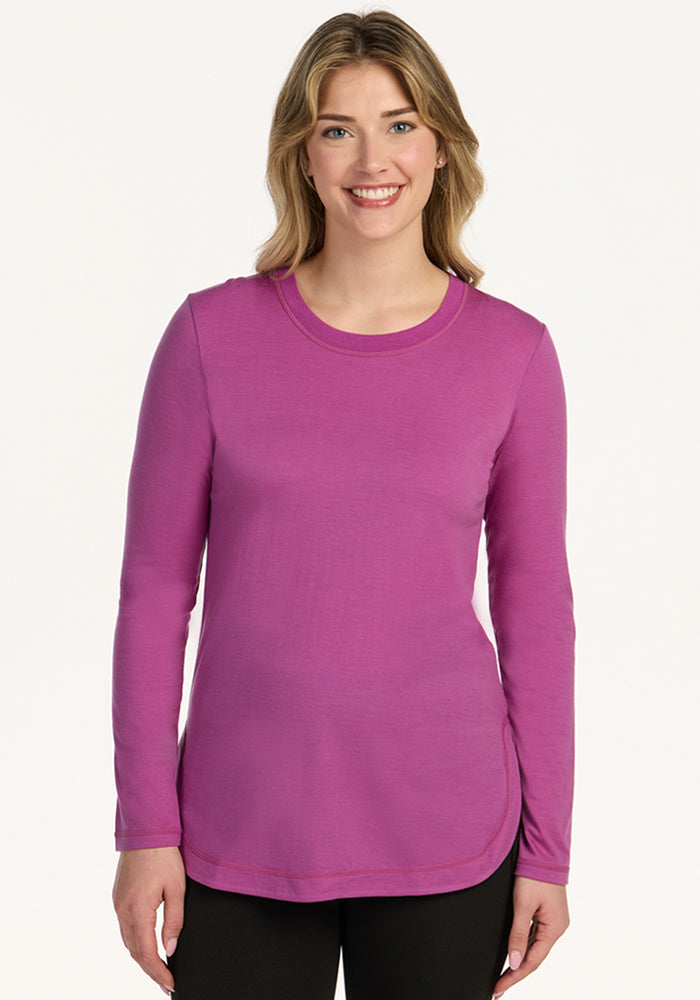 Woman smiling in a Woolx Hazel Tunic in Purple Wine and black pants, standing against a plain white background.