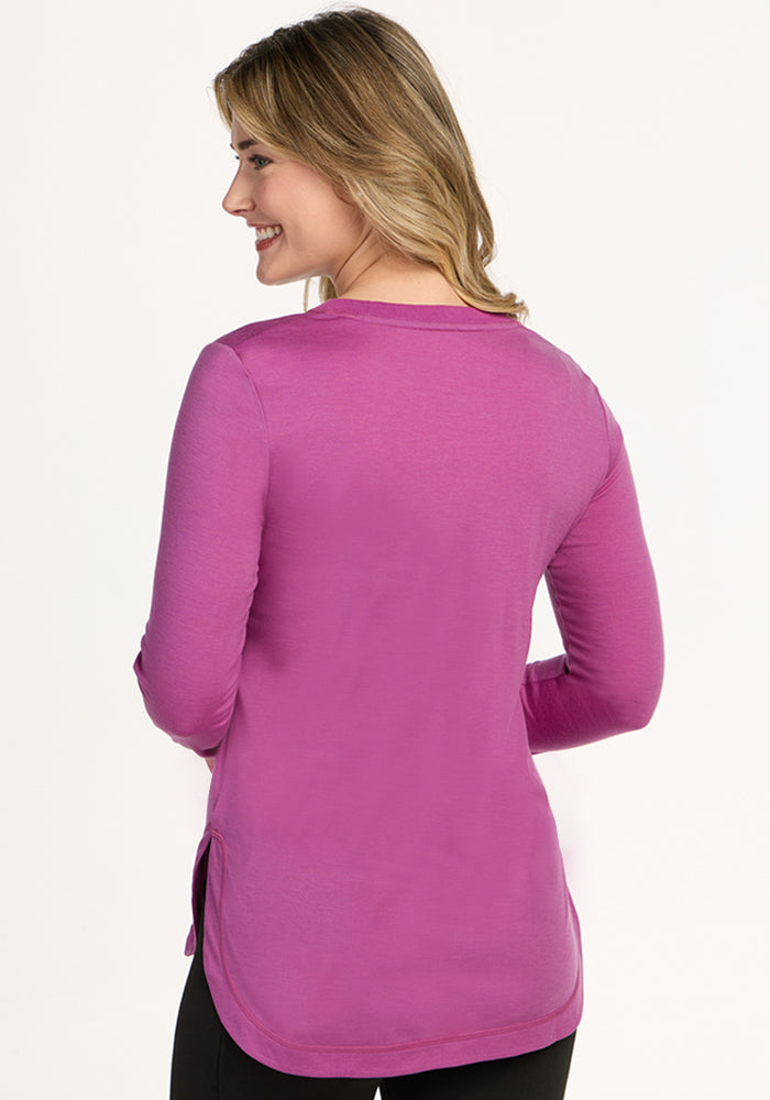 Smiling woman in a Woolx Hazel Tunic, Purple Wine, with long sleeves, back to camera on a light background.