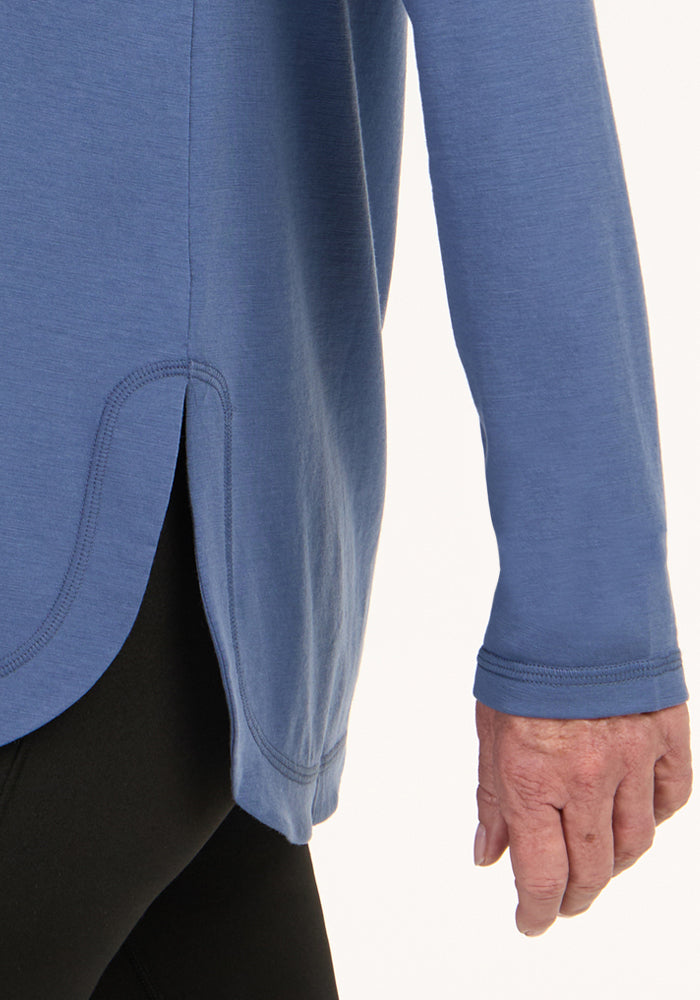 A person in the Woolx Hazel Tunic in Skyline, featuring a blue hue and rounded hem, paired with black pants.