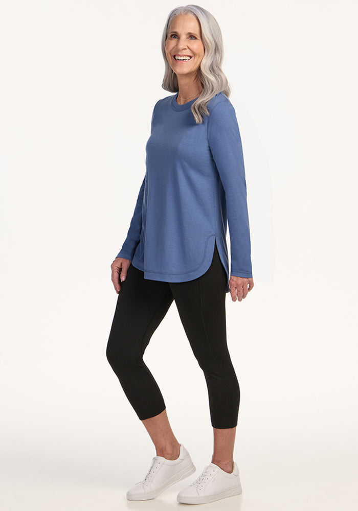 Smiling older woman in the Woolx Hazel Tunic • Final Sale - Skyline, black leggings, and white sneakers.