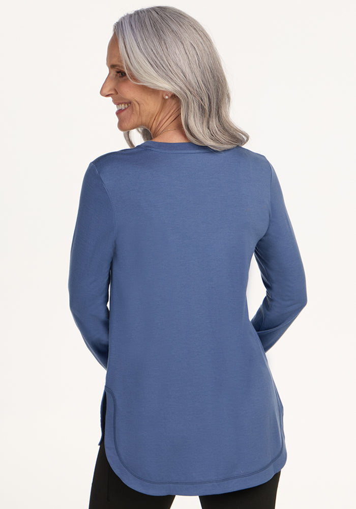 A smiling woman wears the Woolx Hazel Tunic in Skyline, posing with her back to the camera.