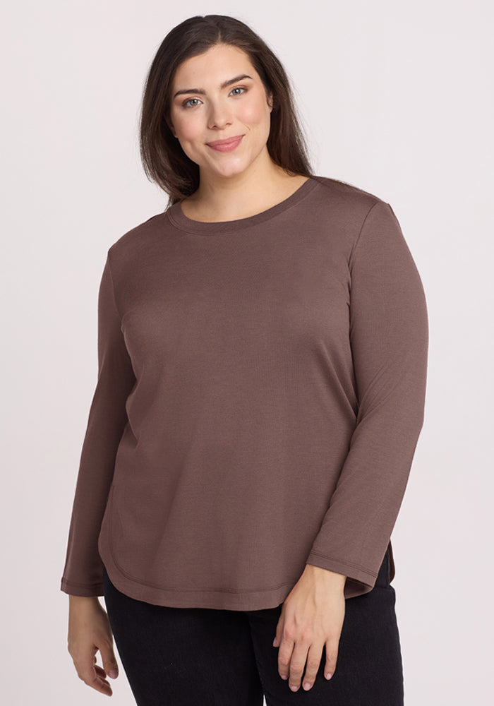 Woman in the Woolx Hazel Tunic in Peppercorn and black pants, smiling in front of a neutral background. | Juliana is 5'10", wearing a size XL