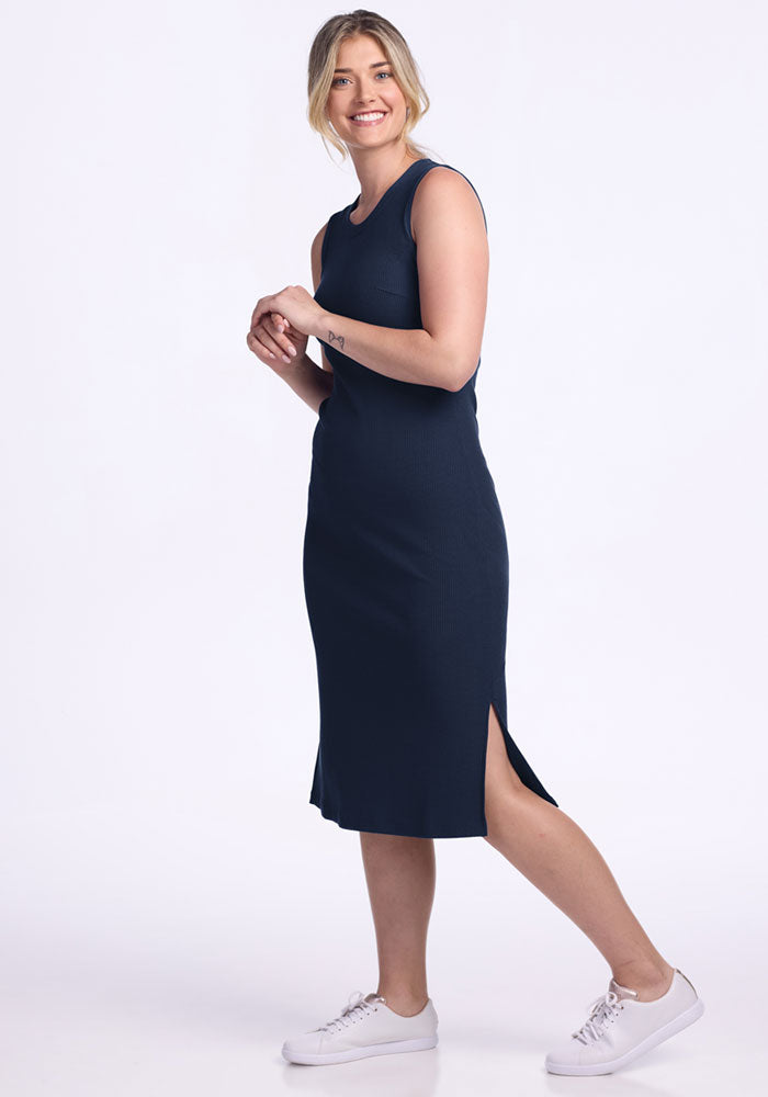 Smiling woman in the Woolx Iris Ribbed Dress • Final Sale - Deep Navy with white sneakers stands against a white background.