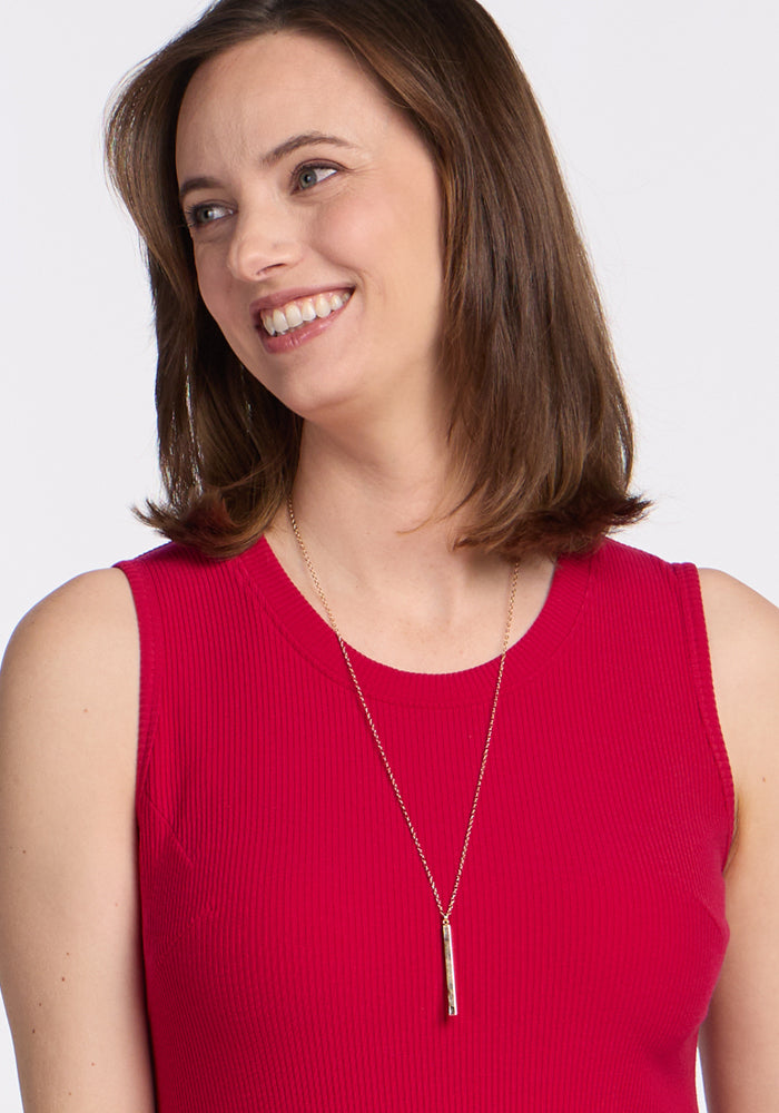 Woman smiles in the Woolx Iris Ribbed Dress in Poppy Spark, styled with a long gold necklace.