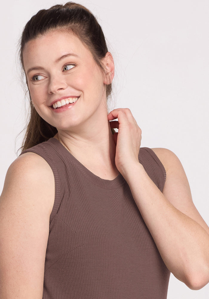 A woman with long brown hair smiles, wearing the Woolx Iris Ribbed Dress in Peppercorn against a light background.