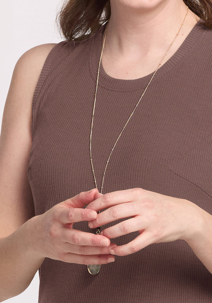 A person in the Woolx Iris Ribbed Dress - Peppercorn holds a pendant necklace, visible from shoulders to waist.