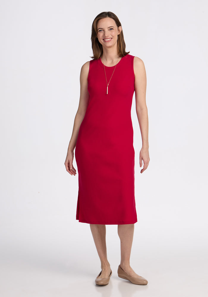 Woman wears Woolx Iris Ribbed Dress in Poppy Spark, sleeveless and knee-length, with a gold necklace and beige flats.