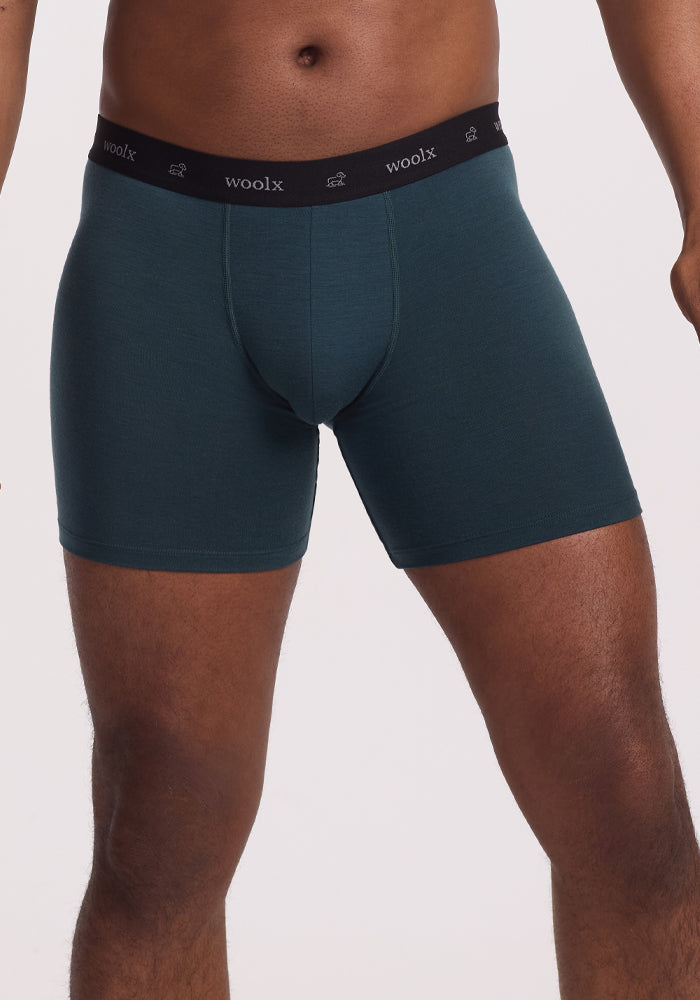 A person wears Enchanted Forest Jazzy No Fly Boxer Briefs with a black waistband featuring "woolx" in white. The image highlights the lower torso and legs against a plain white backdrop, showcasing the comfort and fit of Woolx DuraLite® Fabric.
