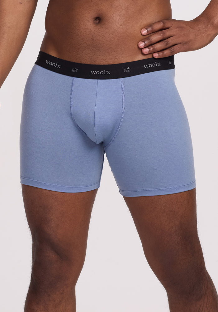 A person models Jazzy No Fly Boxer Briefs—Stonewash by Woolx, showcasing light blue men's underwear with a black "Woolx" waistband and white sheep icons. The image is cropped to the torso and upper thighs.