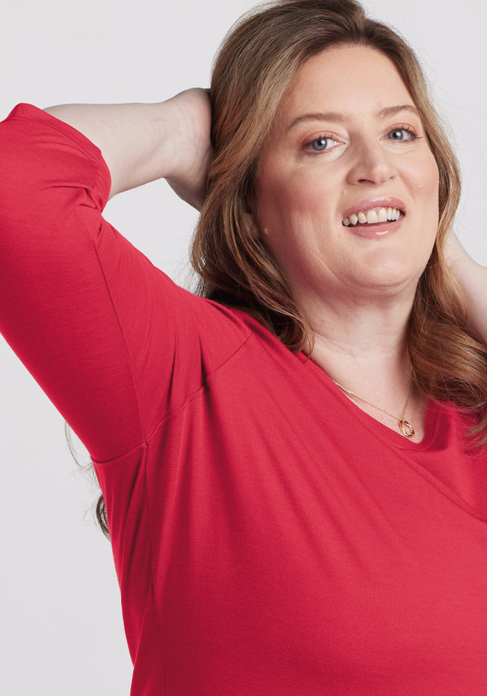 Smiling woman in a Woolx Jenny 3/4 Sleeve Crew Neck - Berry Ice Pop, one arm behind her head, light background.