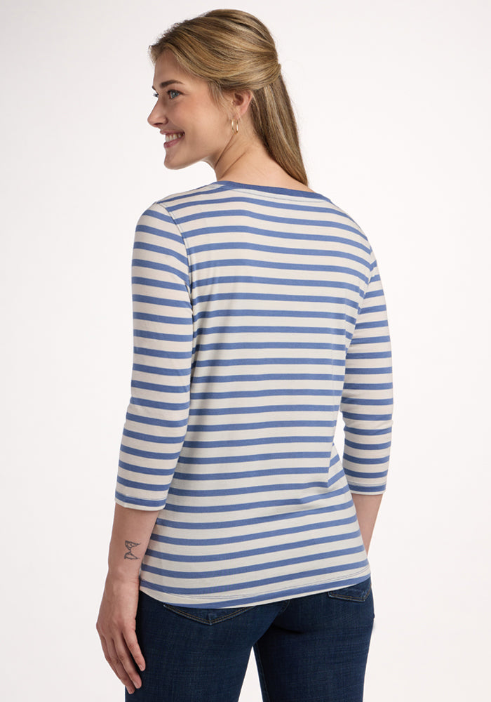 A woman with long, light brown hair in a ponytail smiles as she faces away from the camera, wearing Woolx's Jenny 3/4 Sleeve Crew Neck in Blue Sand Stripe and dark jeans.