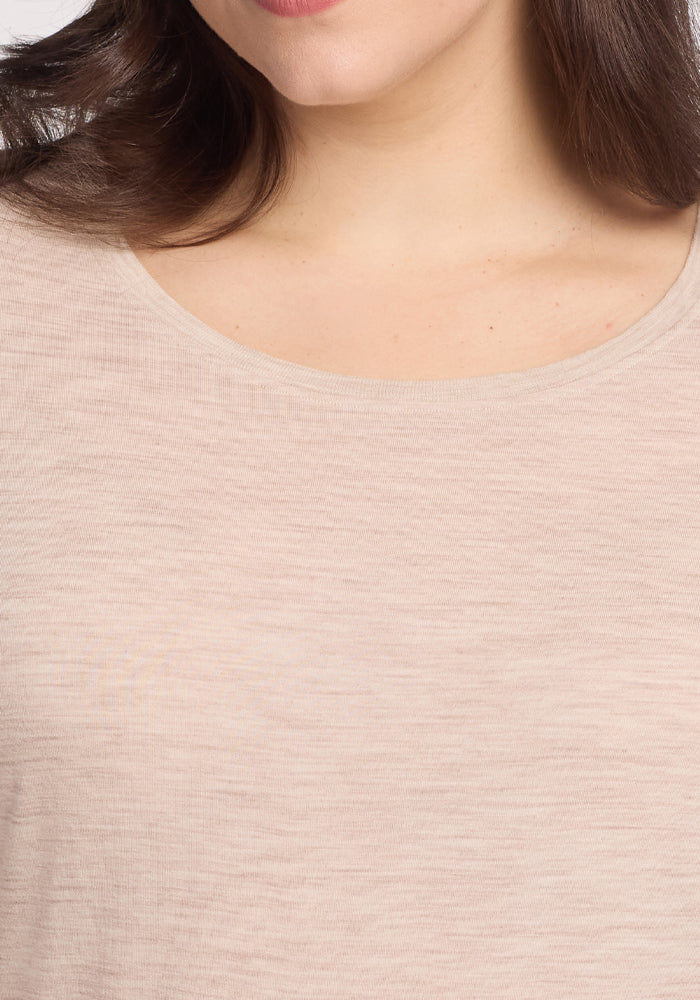 A close-up of a person wearing the Woolx Jenny 3/4 Sleeve Crew Neck in Cream Heather highlights the lightweight texture of the fabric. The image focuses on the upper chest and neckline, with their hair visible on one side.