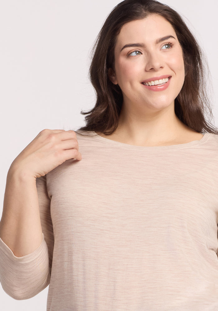A person with long brown hair smiles and looks to the side, wearing a cream heather Jenny 3/4 Sleeve Crew Neck by Woolx. The background is plain and light-colored.