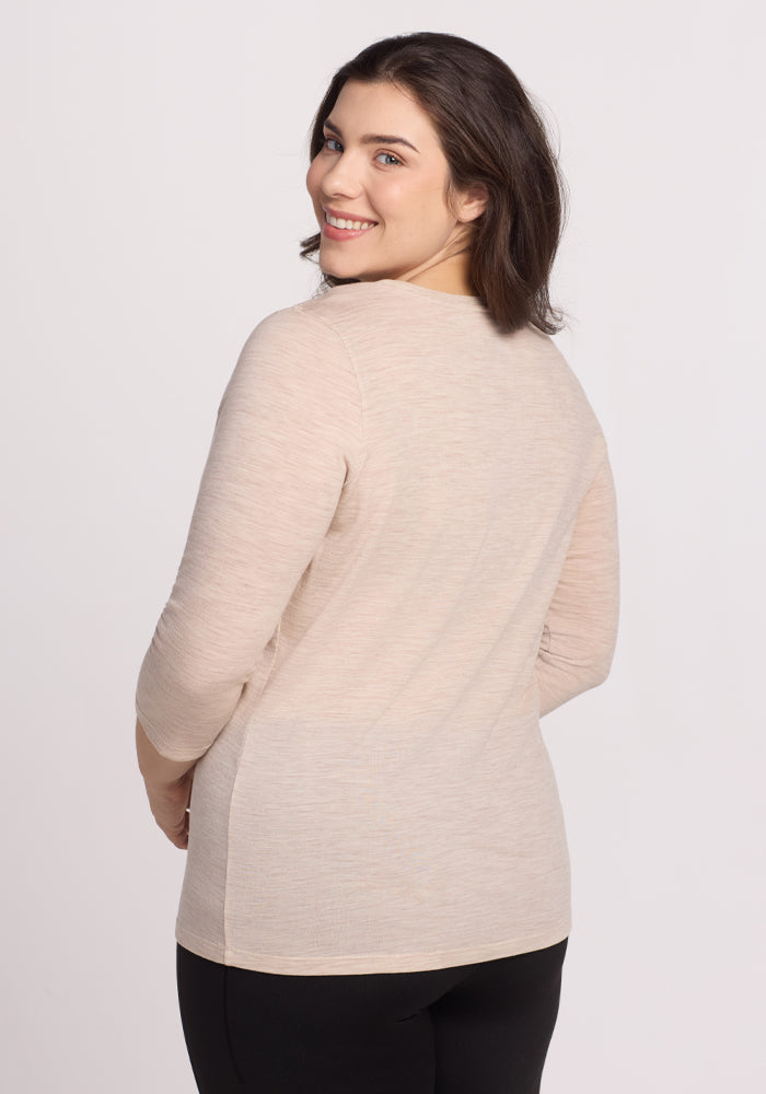 A person with long dark hair, smiling and facing the camera, wears a lightweight Jenny 3/4 Sleeve Crew Neck in Cream Heather from Woolx, paired with black pants against a plain white backdrop.