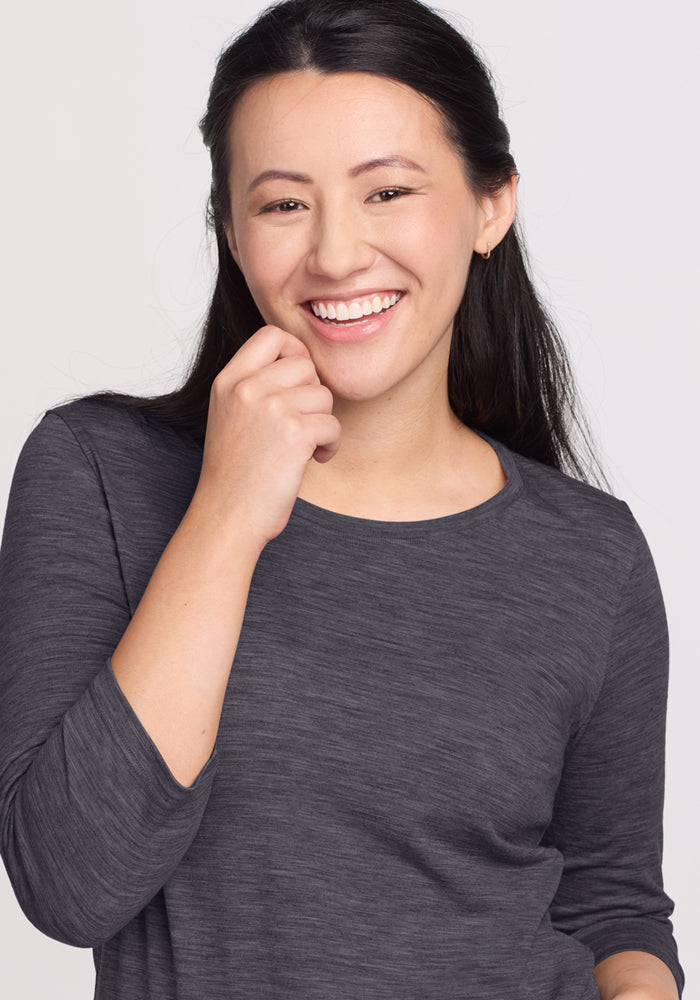 Smiling woman with long dark hair wears Woolx Jenny 3/4 Sleeve Crew Neck in Cinder Melange against a light background.