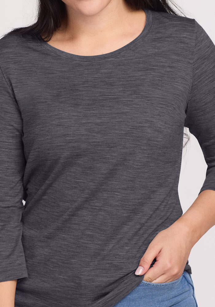 Woman wears a Woolx Jenny 3/4 Sleeve Crew Neck in Cinder Melange with blue pants, holding her shirt hem.