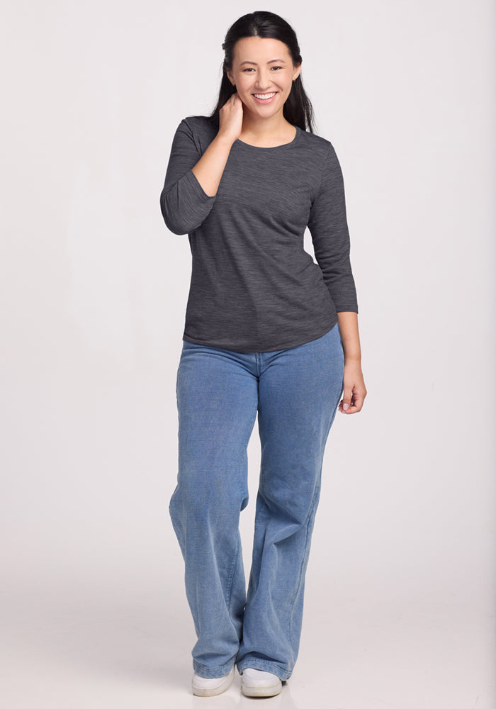 Woman smiling in a Woolx Jenny 3/4 Sleeve Crew Neck in Cinder Melange and light blue jeans against a white background.
