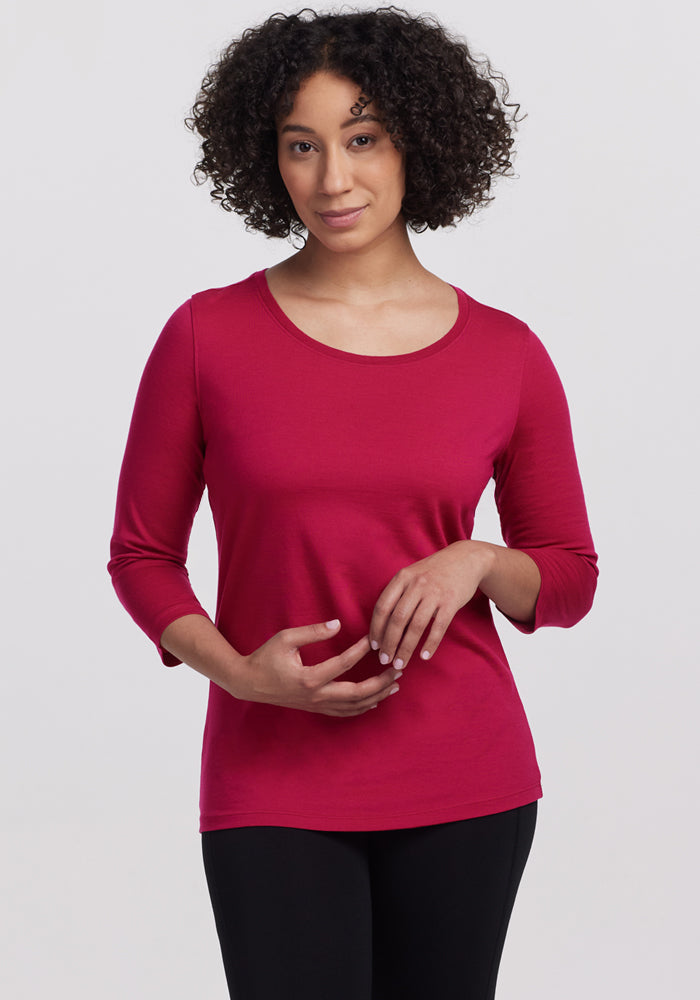 Woman with curly hair wears the Woolx Jenny 3/4 Sleeve Crew Neck in Poppy Spark and black pants, against a light background.