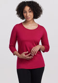Woman with curly hair wears the Woolx Jenny 3/4 Sleeve Crew Neck in Poppy Spark and black pants, against a light background.