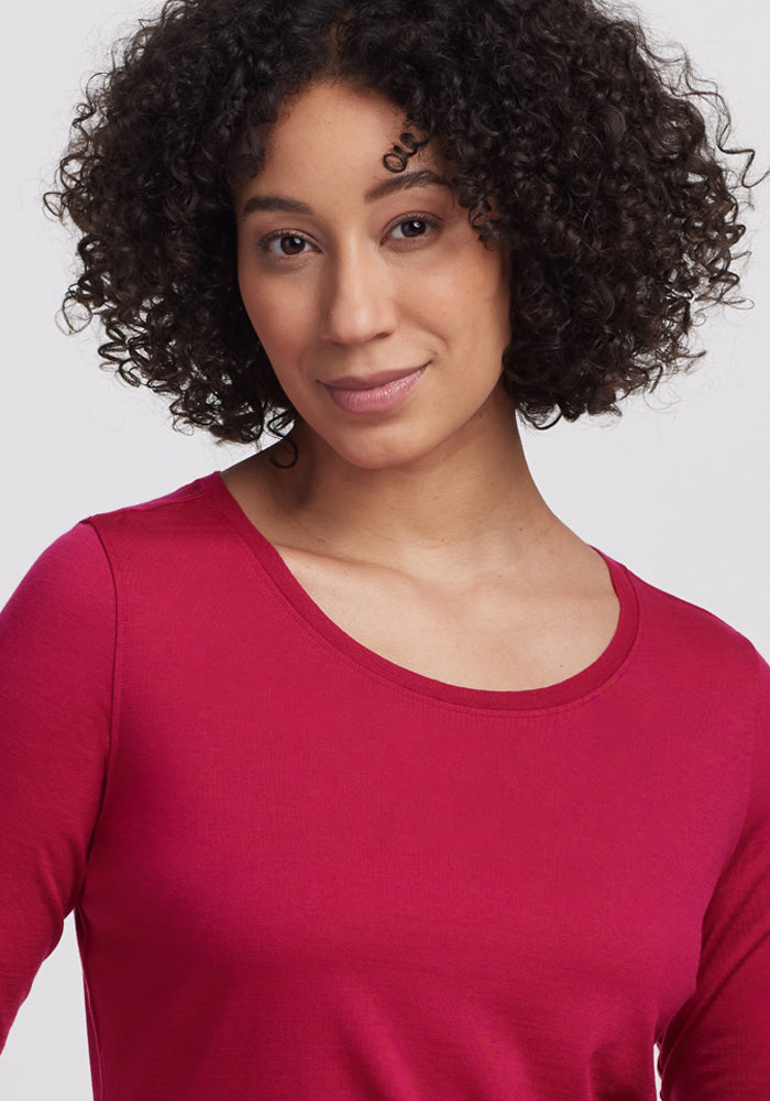 Smiling woman with curly dark hair in Woolx Jenny 3/4 Sleeve Crew Neck - Poppy Spark, against a plain background.