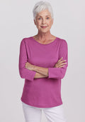 Older woman with short white hair smiles in a Woolx Jenny 3/4 Sleeve Crew Neck in Purple Wine, arms crossed.