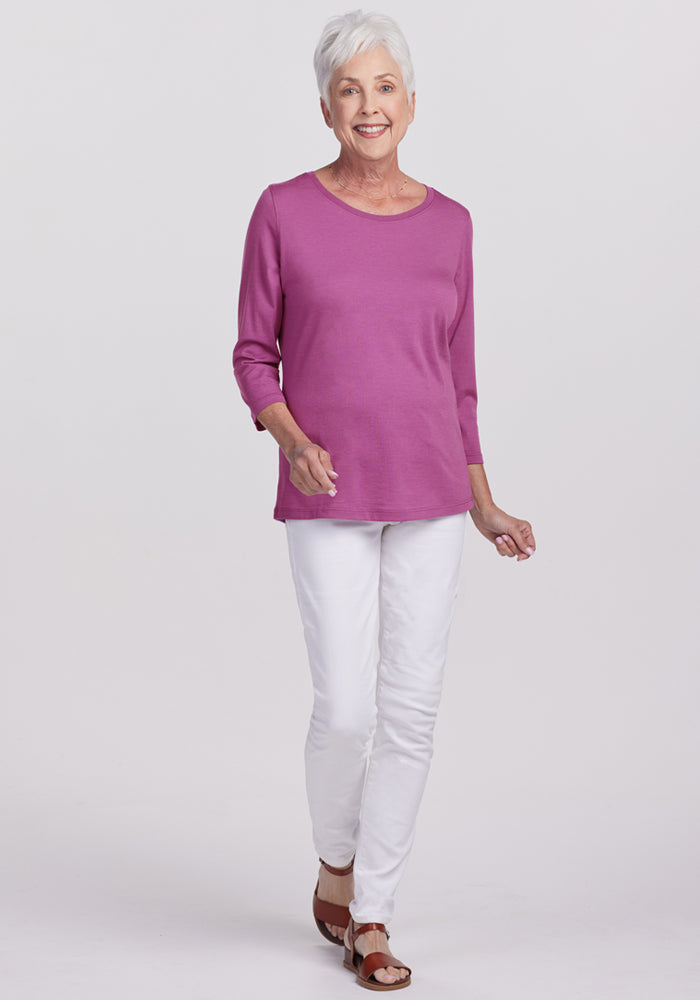 Smiling older woman in a Woolx Jenny 3/4 Sleeve Crew Neck in Purple Wine, with white pants and sandals.