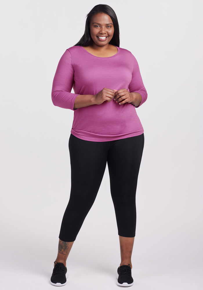 Woman smiling in a Woolx Jenny 3/4 Sleeve Crew Neck in Purple Wine, black leggings, and sneakers against a white background.