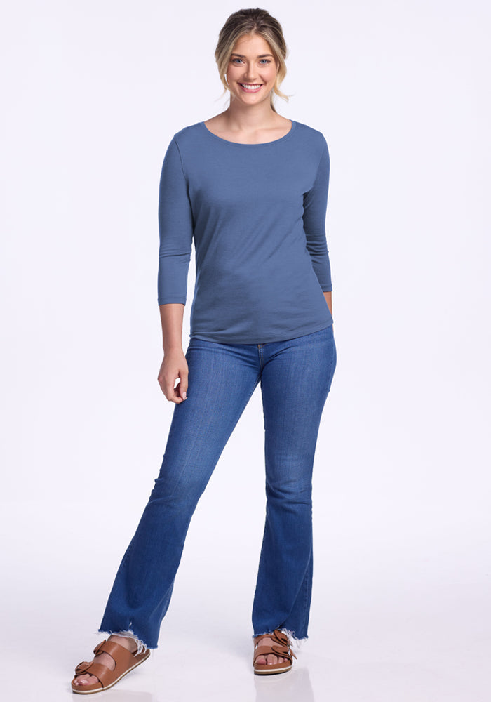 Woman smiling in a blue Woolx Jenny 3/4 Sleeve Crew Neck, jeans, and brown sandals against a white background.
