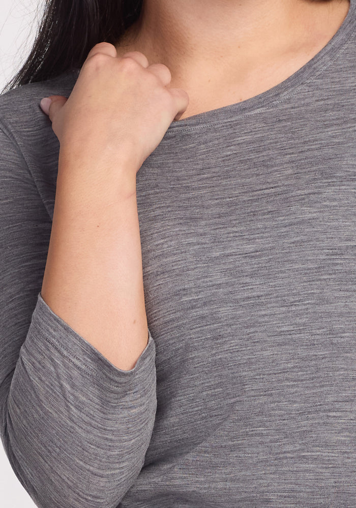 A person wearing the Woolx Jenny 3/4 Sleeve Crew Neck in Graphite Heather rests their left hand near their collarbone. The image is cropped to feature only the upper torso, arm, and part of the neck.
