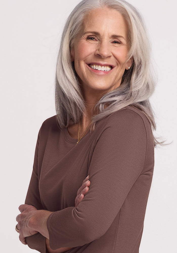 Smiling older woman with long gray hair wears the Woolx Jenny 3/4 Sleeve Crew Neck in Peppercorn, arms crossed.