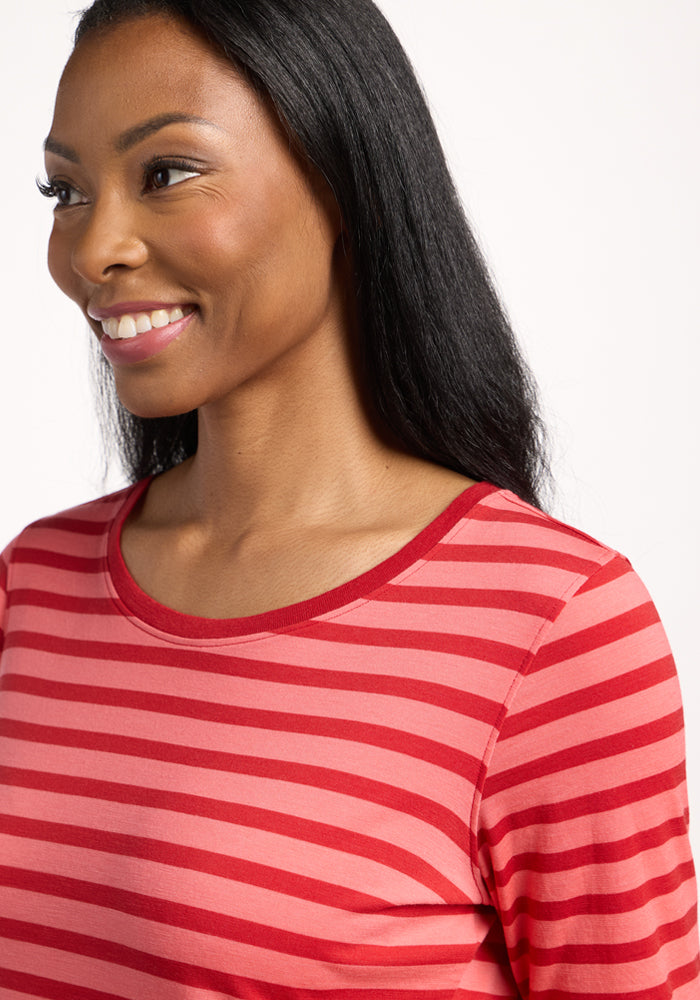 A woman with long dark hair smiles while looking to the side, wearing the Woolx Jenny 3/4 Sleeve Crew Neck in Wildberry Stripe. The lightweight Merino wool shirt features red and pink stripes with a red collar against a plain white background.