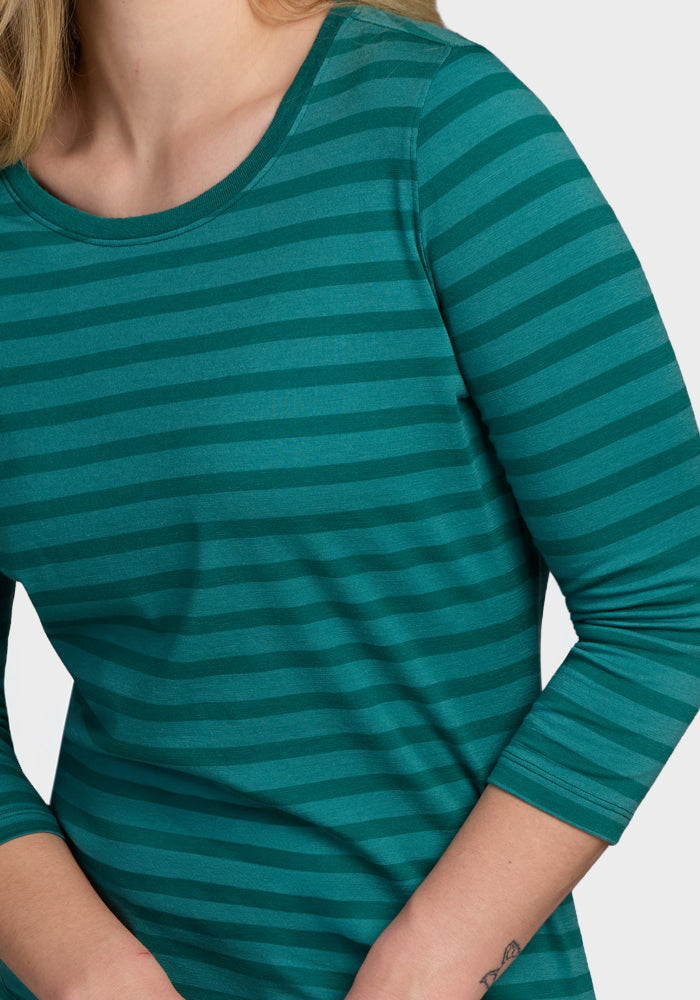 A person is shown from the upper torso wearing the Woolx Jenny 3/4 Sleeve Crew Neck in Woodland Stripe, featuring green and teal stripes with lightweight merino wool fabric.