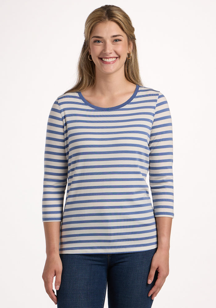A smiling woman with long blonde hair models the Woolx Jenny 3/4 Sleeve Crew Neck in Blue Sand Stripe with blue jeans, standing against a plain white background. | Ariana is 5'11", wearing a size S