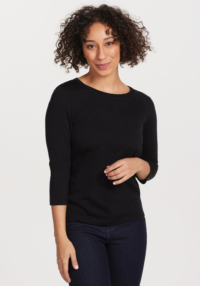 A person with curly hair wearing the Woolx Jenny 3/4 Sleeve Crew Neck in black smiles while standing against a white background, showcasing this versatile wardrobe staple. | Tori is 5'7", wearing a size S