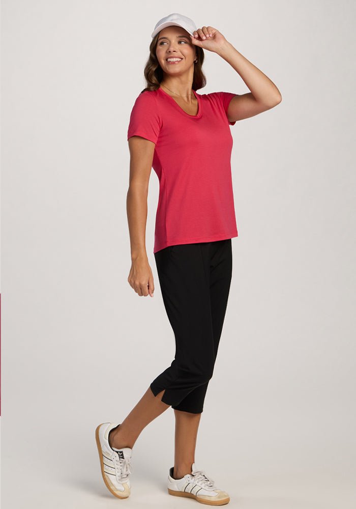 Woman wearing Woolx Junie V Neck in Berry Ice Pop, smiling and posing confidently in black capris and white sneakers.