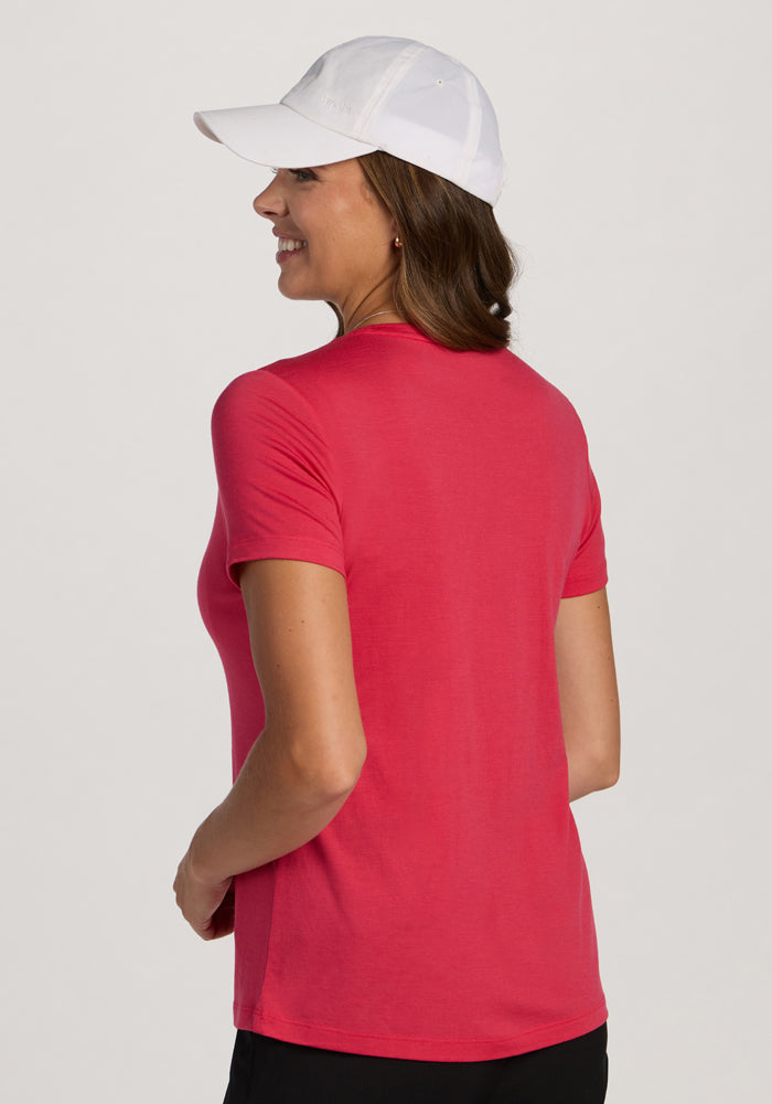 Woman in a Woolx Junie V Neck - Berry Ice Pop tee and white cap, smiling and facing away from the camera.