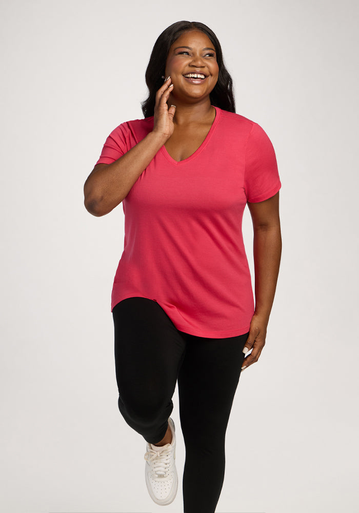 Woman in Woolx Junie V Neck - Berry Ice Pop tee and black pants poses on one leg against a white background.