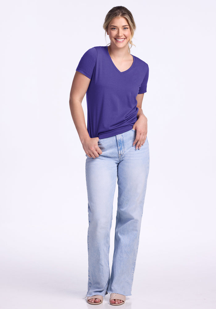 Smiling woman wears the Woolx Junie V Neck - Berry Indigo and light blue jeans on a white background.