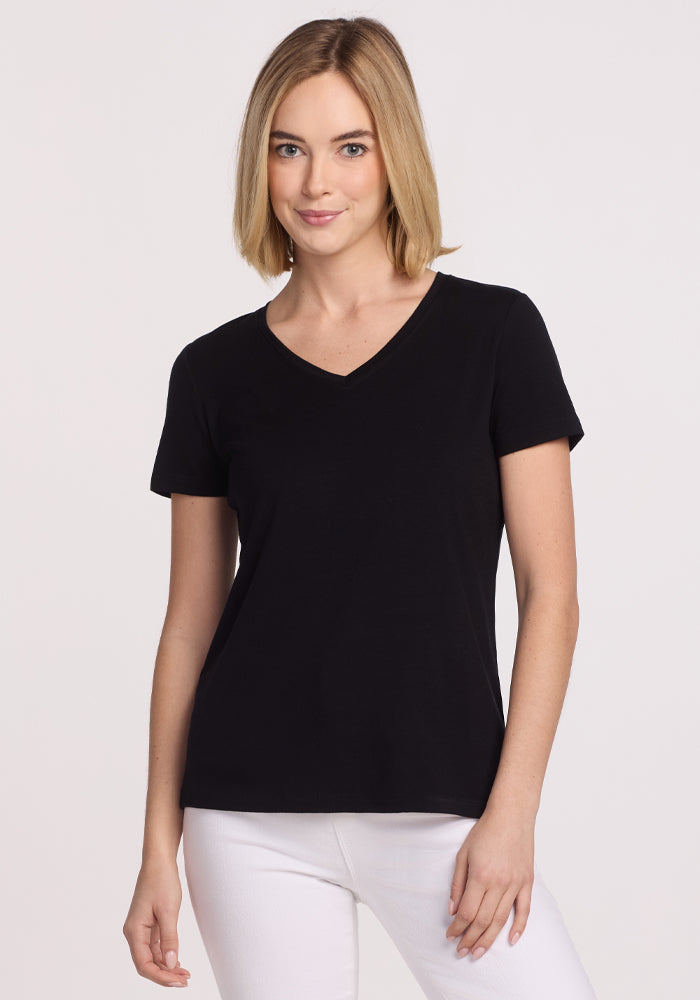 A woman with blonde, shoulder-length hair wears the Woolx Junie V Neck in black and white pants, standing against a plain light background and smiling slightly.