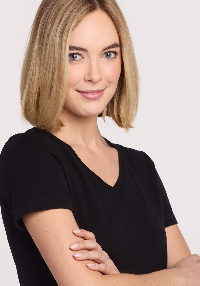 A woman with straight blonde hair, wearing the Woolx Junie V Neck - Black women's relaxed-fit Merino wool tee, stands with her arms crossed and smiles slightly at the camera against a plain light background.